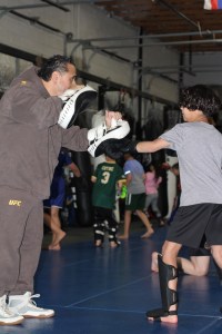 A coach holding pads while a child practices punching at Uprising MMA